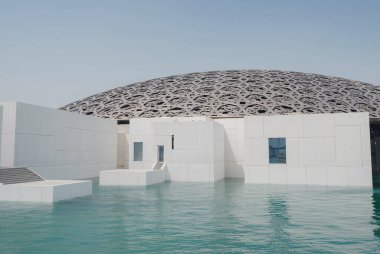 Abu Dabi, BAE - 21 Mart 2023 Louvre Abu Dabi ünlü müzesinin dışı. Zümrüt yeşili hendeği çevreleyen düz beyaz duvarlar süslü bir kubbe çatısı ile kaplı.