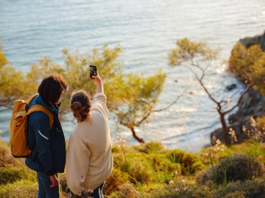 Türkiye gezisi, iki kadın gün batımının keyfini çıkarıyor ve Fethiye şehrinde selfie çekiyor. Birlik, akıl sağlığı, ekolojik seyahat. Dağlarda yürüyüş, seyahat, güzel anlar, dijital detoks.