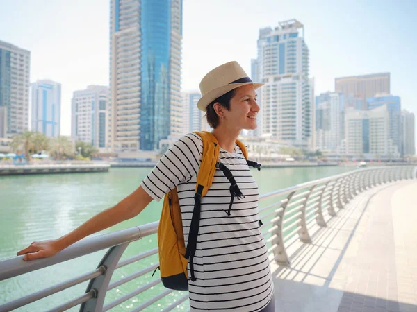 ドバイマリーナ地区の遊歩道を歩く黄色のバックパックを持つ魅力的な旅行者アジアの女性 アラブ首長国連邦の旅行先と観光ライフスタイル — ストック写真