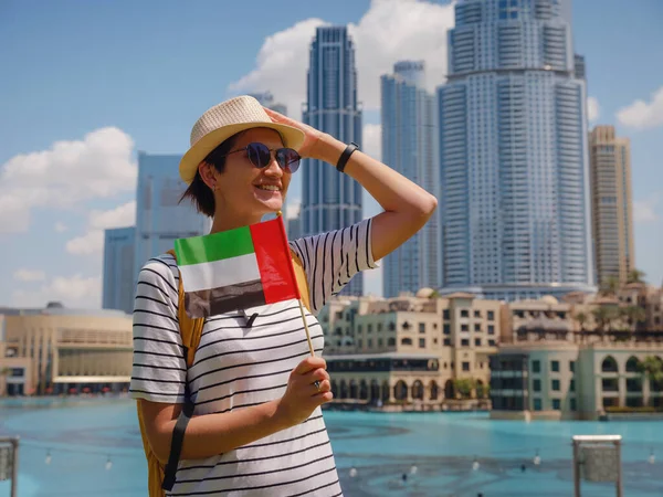 在阿拉伯联合酋长国旅途愉快 在阳光明媚的夏日 身穿黄色背包 打着阿拉伯联合酋长国国旗的年轻女子在迪拜市区散步 — 图库照片