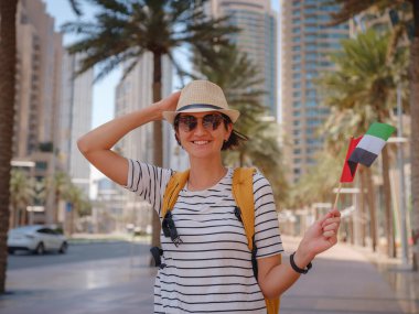 Birleşik Arap Emirlikleri 'nde iyi yolculuklar. Üzerinde Birleşik Arap Emirlikleri bayrağı olan sarı sırt çantalı genç bir kadın güneşli yaz gününde Dubai 'de yürüyor..