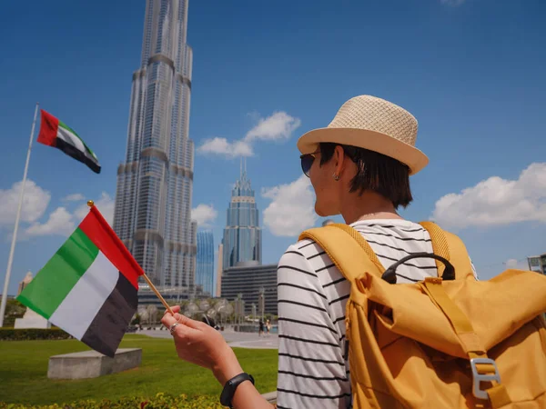 アラブ首長国連邦での旅行をお楽しみください 夏の晴れた日にドバイのダウンタウンを歩くアラブ首長国連邦の旗と黄色のバックパックを持つ若い女性 — ストック写真