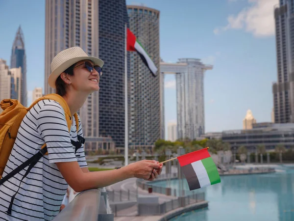 アラブ首長国連邦での旅行をお楽しみください 夏の晴れた日にドバイのダウンタウンを歩くアラブ首長国連邦の旗と黄色のバックパックを持つ若い女性 — ストック写真