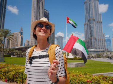 Birleşik Arap Emirlikleri 'nde iyi yolculuklar. Üzerinde Birleşik Arap Emirlikleri bayrağı olan sarı sırt çantalı genç bir kadın güneşli yaz gününde Dubai 'de yürüyor..