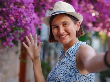 Blooming bougainvillea, streets of the old town of Bodrum, Turkey. Happy traveler woman in white elegant outfit walking by romantic streets . Summer travelling