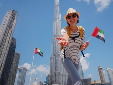 Birleşik Arap Emirlikleri 'nde iyi yolculuklar. Üzerinde Birleşik Arap Emirlikleri bayrağı olan sarı sırt çantalı genç bir kadın güneşli yaz gününde Dubai 'de yürüyor..