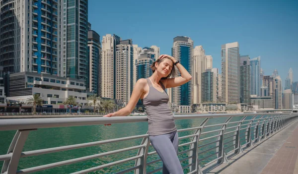 美丽的年轻女子站在迪拜码头的天际线 早上在城里跑步后休息一下 健身后心满意足妇女的画像 — 图库照片