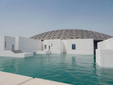 Abu Dabi, BAE - 21 Mart 2023 Louvre Abu Dabi ünlü müzesinin dışı. Zümrüt yeşili hendeği çevreleyen düz beyaz duvarlar süslü bir kubbe çatısı ile kaplı.