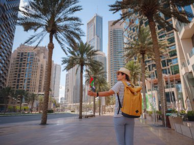 Birleşik Arap Emirlikleri 'nde iyi yolculuklar. Güneşli yaz gününde Dubai şehir merkezinde sarı sırt çantalı genç bir kadın yürüyor. Arkadan ya da arkadan görünüm