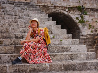 Kırmızı elbiseli genç Asyalı kadın Rodos sokaklarında yürüyor. Rhodes kalesindeki eski evlerin merdivenlerinde dinlenen bir kadın. Turizm, tatil ve keşif konsepti, Güney Avrupa 'yı ziyaret eden kadın gezgin.