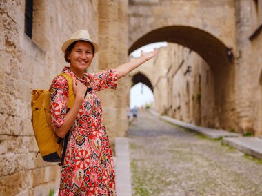 Yunanistan 'ın Rodos adasına yaz gezisi. Etnik kırmızı elbiseli genç Asyalı kadın Kale Şövalyeleri Sokağı 'nda yürüyor. Bayan gezgin Güney Avrupa 'yı ziyaret ediyor. Unesco Dünya Mirası Bölgesi.