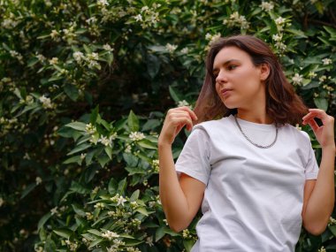 Koyu kıvırcık saçlı, mükemmel tenli, beyaz tişörtlü, çiçek açan turuncu bahçenin yanında poz veren güzel bir genç kadın. Çıplak makyaj malzemesi. Alerji sezonu, antihistaminler. Aroma doğal parfümleri yağlar.