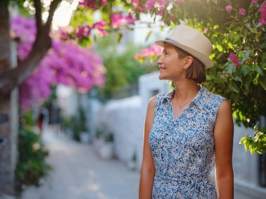 Çiçekli begonviller, eski Bodrum kasabasının sokakları, Türkiye. Romantik caddelerde yürüyen beyaz şık elbiseli mutlu bir gezgin kadın. Yaz gezisi