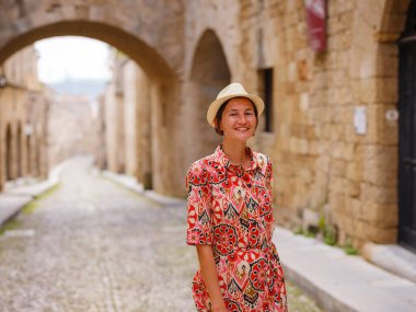 Yunanistan 'ın Rodos adasına yaz gezisi. Etnik kırmızı elbiseli genç Asyalı kadın Kale Şövalyeleri Sokağı 'nda yürüyor. Bayan gezgin Güney Avrupa 'yı ziyaret ediyor. Unesco Dünya Mirası Bölgesi.