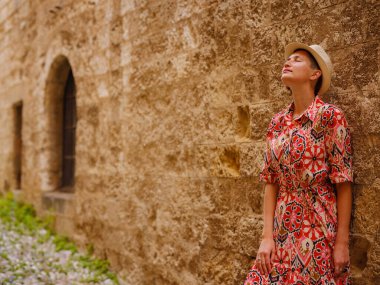 Yunanistan 'ın Rodos adasına yaz gezisi. Etnik kırmızı elbiseli genç Asyalı kadın Rodos sokaklarında yürüyor. Turizm, tatil ve keşif konsepti, Güney Avrupa 'yı ziyaret eden kadın gezgin.