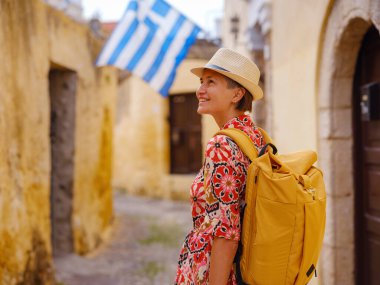 Etnik kırmızı elbiseli genç Asyalı kadın yürür ve eski şehrin sıcacık dar sokaklarına bakar. Turizm, tatil ve keşif konsepti, Güney Avrupa, Rodos Adası, Yunanistan 'ı ziyaret eden kadın gezgin.