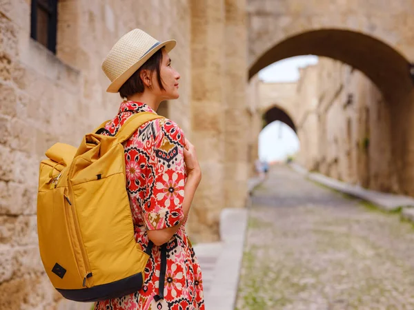 stock image summer trip to Rhodes island, Greece. Young Asian woman in ethnic red dress walks Street of Knights of Fortifications castle. female traveler visiting southern Europe. Unesco world heritage site.