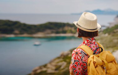 Şapkalı Asyalı kadın Akdeniz 'deki gök mavisi Bay manzarasına bakıyor. Seyahat ve tatil konsepti. Anthony Quinn körfezi, Yunanistan 'ın Rodos adasında berrak suyla birlikte. En güzel kumsal.