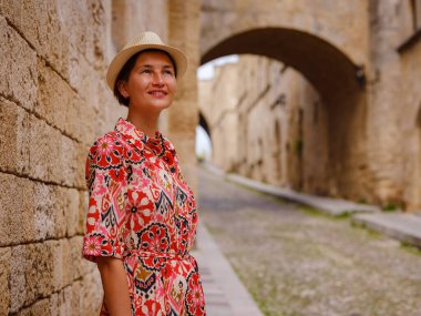 Yunanistan 'ın Rodos adasına yaz gezisi. Etnik kırmızı elbiseli genç Asyalı kadın Kale Şövalyeleri Sokağı 'nda yürüyor. Bayan gezgin Güney Avrupa 'yı ziyaret ediyor. Unesco Dünya Mirası Bölgesi.