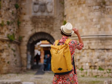 Yunanistan 'ın Rodos adasına yaz gezisi. Etnik kırmızı elbiseli genç Asyalı kadın Rodos sokaklarında yürüyor. Bayan gezgin Güney Avrupa 'yı ziyaret ediyor. Unesco Dünya Mirası Bölgesi.