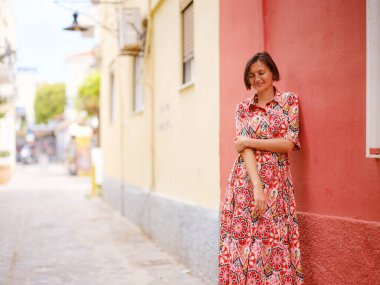 Yunanistan 'ın Rodos adasına yaz gezisi. Etnik kırmızı elbiseli genç Asyalı kadın Rodos şehrinin rahat renkli sokaklarında yürüyor. Turizm, tatil, solo seyahat ve keşif konsepti