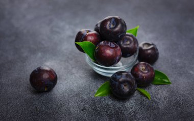 Koyu arkaplanda tatlı erikler. Yapraklı taze mavi erikler. Gıda meyvesi arka planı. Yaz kartpostalı. Bahçede hasat, erik hasadı.