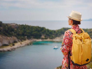 Şapkalı Asyalı kadın Akdeniz 'deki gök mavisi Bay manzarasına bakıyor. Seyahat ve tatil konsepti. Anthony Quinn körfezi, Yunanistan 'ın Rodos adasında berrak suyla birlikte. En güzel kumsal.