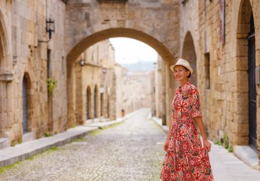 Yunanistan 'ın Rodos adasına yaz gezisi. Etnik kırmızı elbiseli genç Asyalı kadın Kale Şövalyeleri Sokağı 'nda yürüyor. Bayan gezgin Güney Avrupa 'yı ziyaret ediyor. Unesco Dünya Mirası Bölgesi.