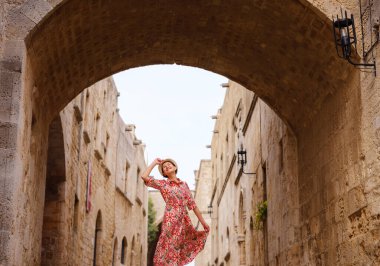 Yunanistan 'ın Rodos adasına yaz gezisi. Etnik kırmızı elbiseli genç Asyalı kadın Kale Şövalyeleri Sokağı 'nda yürüyor. Bayan gezgin Güney Avrupa 'yı ziyaret ediyor. Unesco Dünya Mirası Bölgesi.