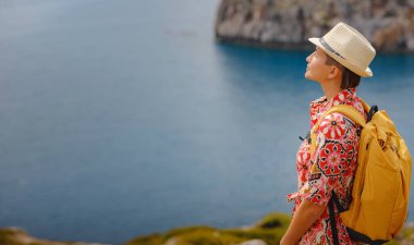 Şapkalı Asyalı kadın Akdeniz 'deki gök mavisi Bay manzarasına bakıyor. Seyahat ve tatil konsepti. Anthony Quinn körfezi, Yunanistan 'ın Rodos adasında berrak suyla birlikte. En güzel kumsal.