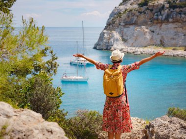 Şapkalı Asyalı kadın Akdeniz 'deki gök mavisi Bay manzarasına bakıyor. Seyahat ve tatil konsepti. Anthony Quinn körfezi, Yunanistan 'ın Rodos adasında berrak suyla birlikte. En güzel kumsal.