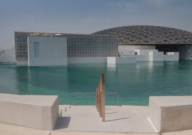 Abu Dabi, BAE - 21 Mart 2023 Louvre Abu Dabi ünlü müzesinin dışı. Zümrüt yeşili hendeği çevreleyen düz beyaz duvarlar süslü bir kubbe çatısı ile kaplı.