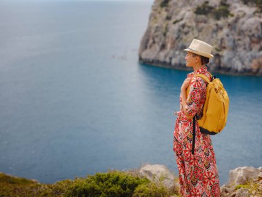 Şapkalı Asyalı kadın Akdeniz 'deki gök mavisi Bay manzarasına bakıyor. Seyahat ve tatil konsepti. Anthony Quinn körfezi, Yunanistan 'ın Rodos adasında berrak suyla birlikte. En güzel kumsal.