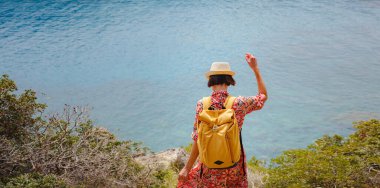 Şapkalı Asyalı kadın Akdeniz 'deki gök mavisi Bay manzarasına bakıyor. Seyahat ve tatil konsepti. Anthony Quinn körfezi, Yunanistan 'ın Rodos adasında berrak suyla birlikte. En güzel kumsal.