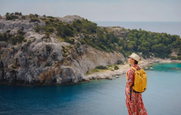 stock image Asian woman in hat look on views of azure Bay in Mediterranean sea. Travel and vacation concept. Anthony Quinn bay with crystal clear water in Rhodes island, Greece. The most beautiful beach.