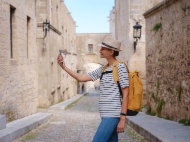 Yunanistan 'ın Rodos adasına yaz gezisi. Genç Asyalı kadın akıllı telefondan fotoğraf çekiyor. Sokak Şövalyeleri Kalesi 'nde yürüyor. Bayan gezgin Güney Avrupa 'yı ziyaret ediyor. Unesco Dünya Mirası Bölgesi