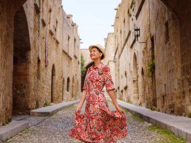 Yunanistan 'ın Rodos adasına yaz gezisi. Etnik kırmızı elbiseli genç Asyalı kadın Kale Şövalyeleri Sokağı 'nda yürüyor. Bayan gezgin Güney Avrupa 'yı ziyaret ediyor. Unesco Dünya Mirası Bölgesi.