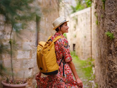 Etnik kırmızı elbiseli genç Asyalı kadın yürür ve eski şehrin sıcacık dar sokaklarına bakar. Turizm, tatil ve keşif konsepti, Güney Avrupa, Rodos Adası, Yunanistan 'ı ziyaret eden kadın gezgin.