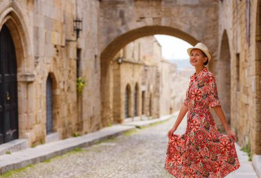 Yunanistan 'ın Rodos adasına yaz gezisi. Etnik kırmızı elbiseli genç Asyalı kadın Kale Şövalyeleri Sokağı 'nda yürüyor. Bayan gezgin Güney Avrupa 'yı ziyaret ediyor. Unesco Dünya Mirası Bölgesi.
