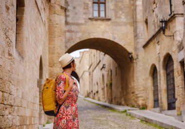 Yunanistan 'ın Rodos adasına yaz gezisi. Etnik kırmızı elbiseli genç Asyalı kadın Kale Şövalyeleri Sokağı 'nda yürüyor. Bayan gezgin Güney Avrupa 'yı ziyaret ediyor. Unesco Dünya Mirası Bölgesi.