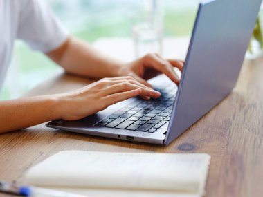 Laptop kullanan ve evde çalışırken gülümseyen gündelik giysili güzel Latin bir kadın. Bayan bilgisayar başında çalışıyor kulaklıkla müzik dinliyor. Klavyede yazılıyor, kapat