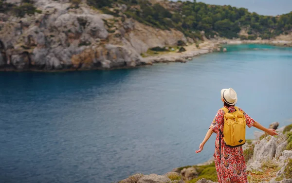 Şapkalı Asyalı kadın Akdeniz 'deki gök mavisi Bay manzarasına bakıyor. Seyahat ve tatil konsepti. Anthony Quinn körfezi, Yunanistan 'ın Rodos adasında berrak suyla birlikte. En güzel kumsal.