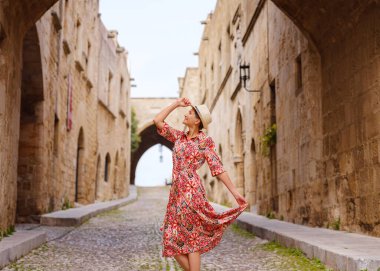 Yunanistan 'ın Rodos adasına yaz gezisi. Etnik kırmızı elbiseli genç Asyalı kadın Kale Şövalyeleri Sokağı 'nda yürüyor. Bayan gezgin Güney Avrupa 'yı ziyaret ediyor. Unesco Dünya Mirası Bölgesi.