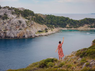 Şapkalı Asyalı kadın Akdeniz 'deki gök mavisi Bay manzarasına bakıyor. Seyahat ve tatil konsepti. Anthony Quinn körfezi, Yunanistan 'ın Rodos adasında berrak suyla birlikte. En güzel kumsal.