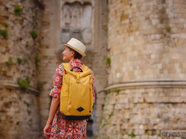 Yunanistan 'ın Rodos adasına yaz gezisi. Etnik kırmızı elbiseli genç Asyalı kadın Rodos sokaklarında yürüyor. Bayan gezgin Güney Avrupa 'yı ziyaret ediyor. Unesco Dünya Mirası Bölgesi.