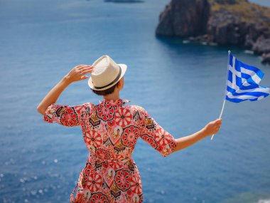 Yunan Adaları 'nda güneşli bir günün tadını çıkaran güzel mutlu kadın. Yunanistan 'a seyahat, turizm sezonu dışında Akdeniz adaları. Ulusal Yunan bayrağıyla gezen genç kadın deniz manzarasının keyfini çıkarıyor