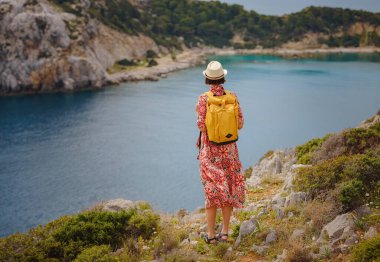 Şapkalı Asyalı kadın Akdeniz 'deki gök mavisi Bay manzarasına bakıyor. Seyahat ve tatil konsepti. Anthony Quinn körfezi, Yunanistan 'ın Rodos adasında berrak suyla birlikte. En güzel kumsal.