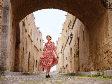 Yunanistan 'ın Rodos adasına yaz gezisi. Etnik kırmızı elbiseli genç Asyalı kadın Kale Şövalyeleri Sokağı 'nda yürüyor. Bayan gezgin Güney Avrupa 'yı ziyaret ediyor. Unesco Dünya Mirası Bölgesi.