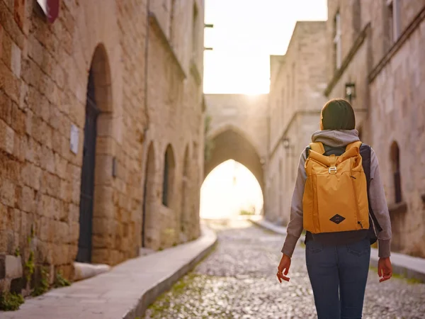 stock image spring or fall trip to Rhodes island, Greece. Young Asian woman walks Street of Knights of Fortifications castle over sunset time. female traveler visiting southern Europe. Unesco world heritage site.