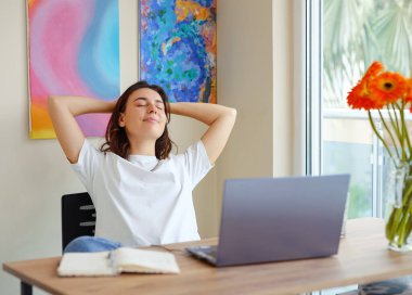 Mutlu Latin kadın ev ofisinde dinleniyor, dizüstü bilgisayarla el ele tutuşuyor, rüya gibi genç bayan işini bitirmiş, iç huzurunu bulmuş başını çevirmiş, gelecek başarı kavramını hayal ediyor.